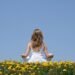 Cultivate mindfulness – woman meditating in a field of yellow flowers under a clear blue sky