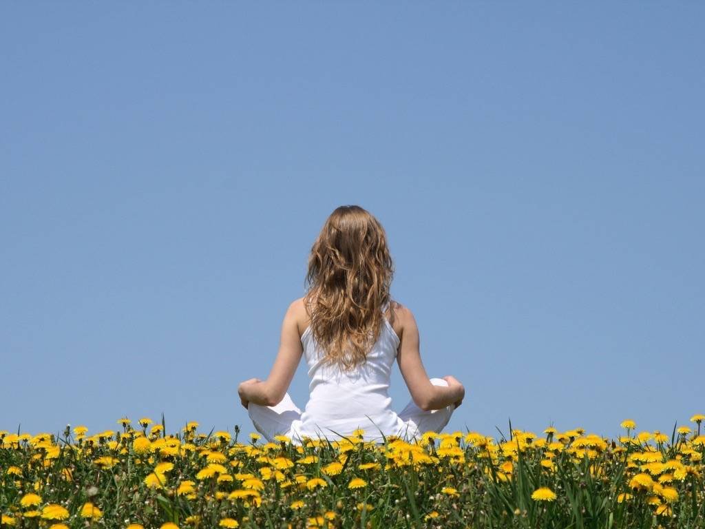 Cultivate mindfulness – woman meditating in a field of yellow flowers under a clear blue sky