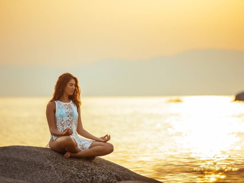 Cultivate mindfulness – woman practicing mindfulness meditation by the sea at sunset