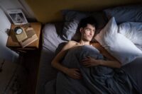 person lying awake in bed at night struggling with how to stop overthinking at night