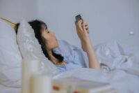 person lying in bed with phone instead of following morning routine ideas