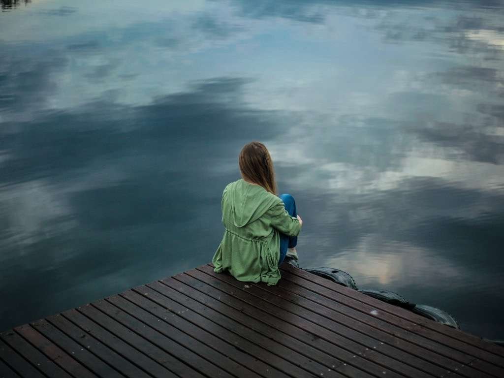 Woman sitting alone by the water feeling depressed and isolated