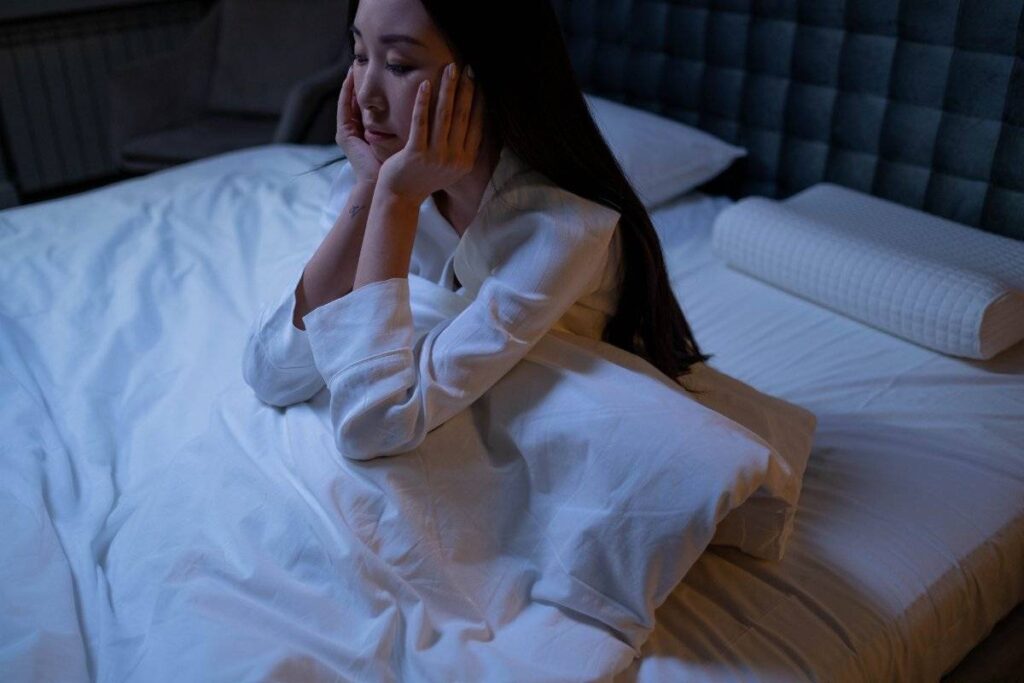 person sitting exhausted in bed showing physical effects of overthinking at night