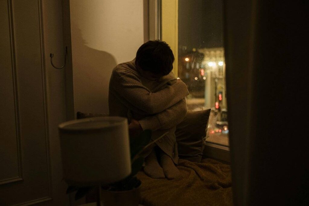 person alone by window at night reflecting on how to deal with loneliness