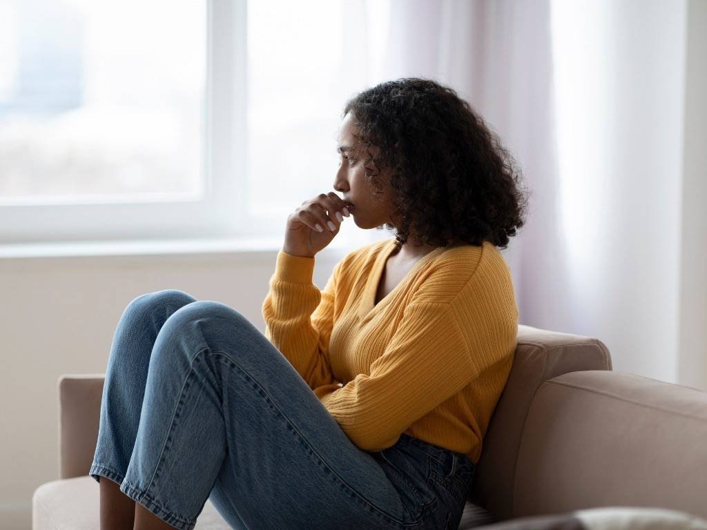 Woman in yellow sweater sitting on couch, looking worried and showing signs of depression