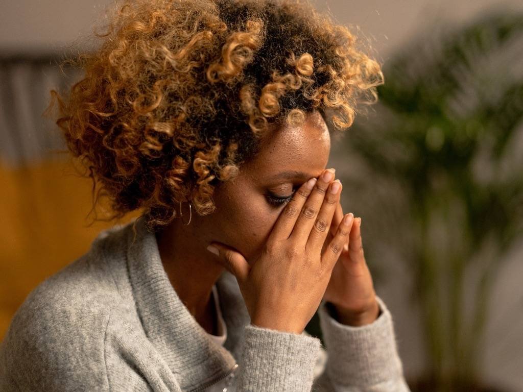 Sad woman with curly hair covering face with hands, showing stress and depression