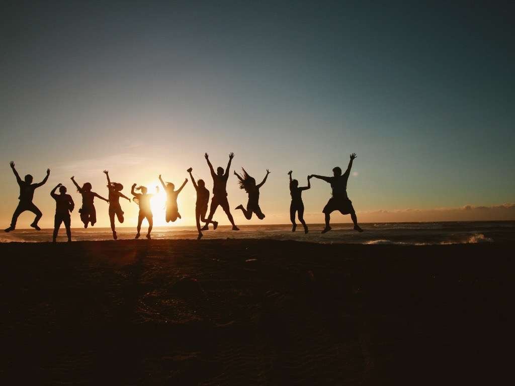 Group of friends jumping on the beach at sunset — representing happiness and positive mental health tips