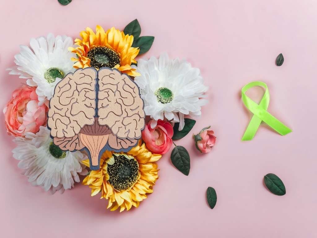 Mental health awareness symbol with brain illustration, green ribbon, and colorful flowers representing hope and emotional well-being.