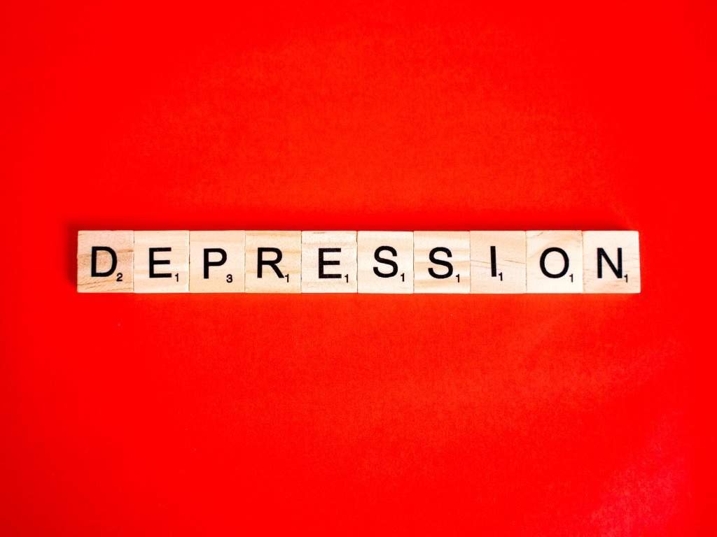 Word “Depression” spelled with wooden Scrabble tiles on a bright red background, symbolizing mental health disorders and emotional struggles.