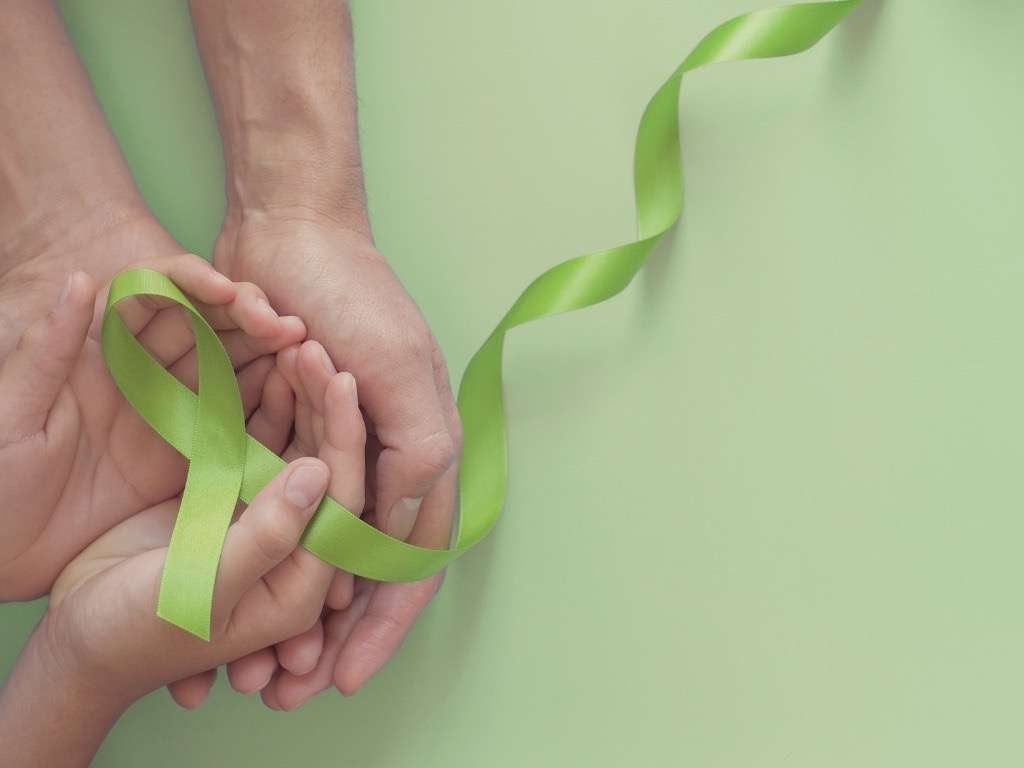Hands holding a green ribbon symbolizing mental health awareness, hope, and support.