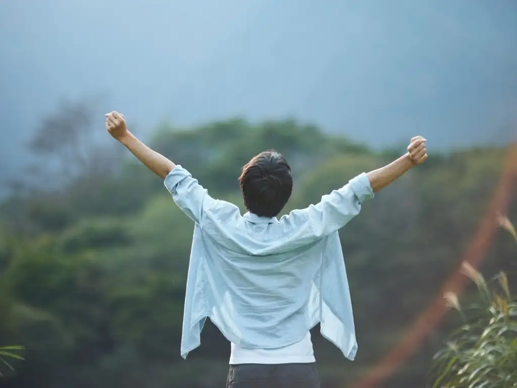Man raising arms in nature symbolizing freedom, success, and personal growth