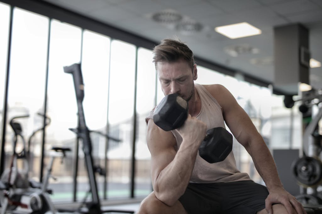 Low angle of powerful male athlete in sportswear performing exercise with heavy metal dumbbell while sitting on bench during workout in modern gym