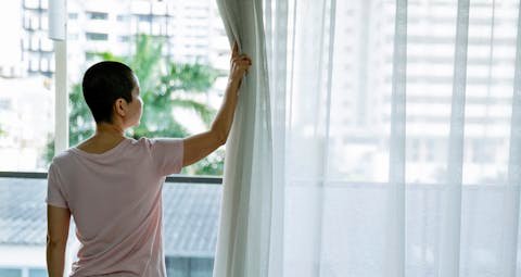 Short haired sick Asian woman opening curtains of windows in hospital