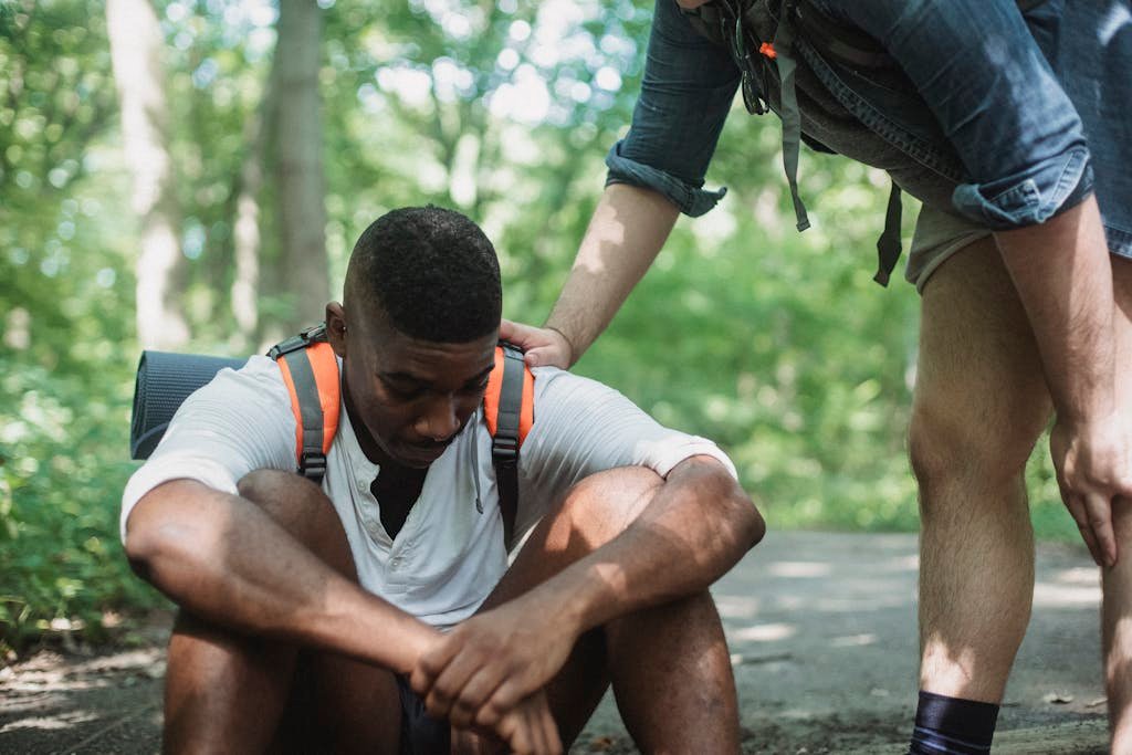 Unhappy black hiker sitting on ground in forest