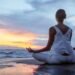 Woman practicing meditation at the beach during sunset for stress relief and better focus