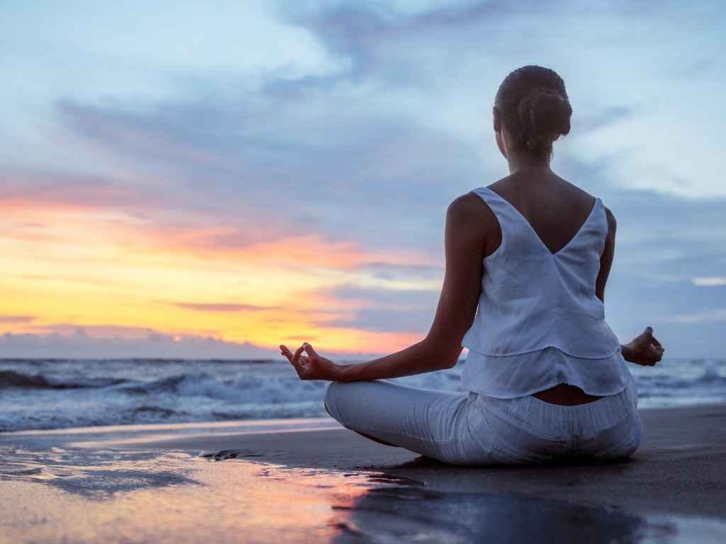 Woman practicing meditation at the beach during sunset for stress relief and better focus