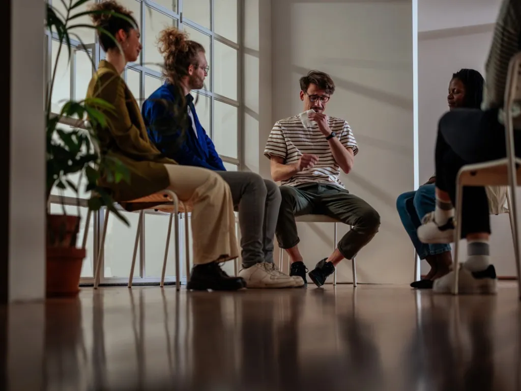 “Group therapy session showing people sharing experiences, representing the benefits of therapy for mental health.