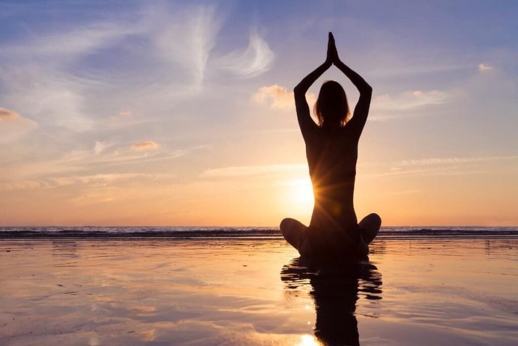 Woman practicing mindfulness meditation at sunrise on the beach for better mental health and well-being
