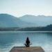 Woman meditating by a peaceful lake with mountains in the background – self-help tools for mental wellness and stress relief