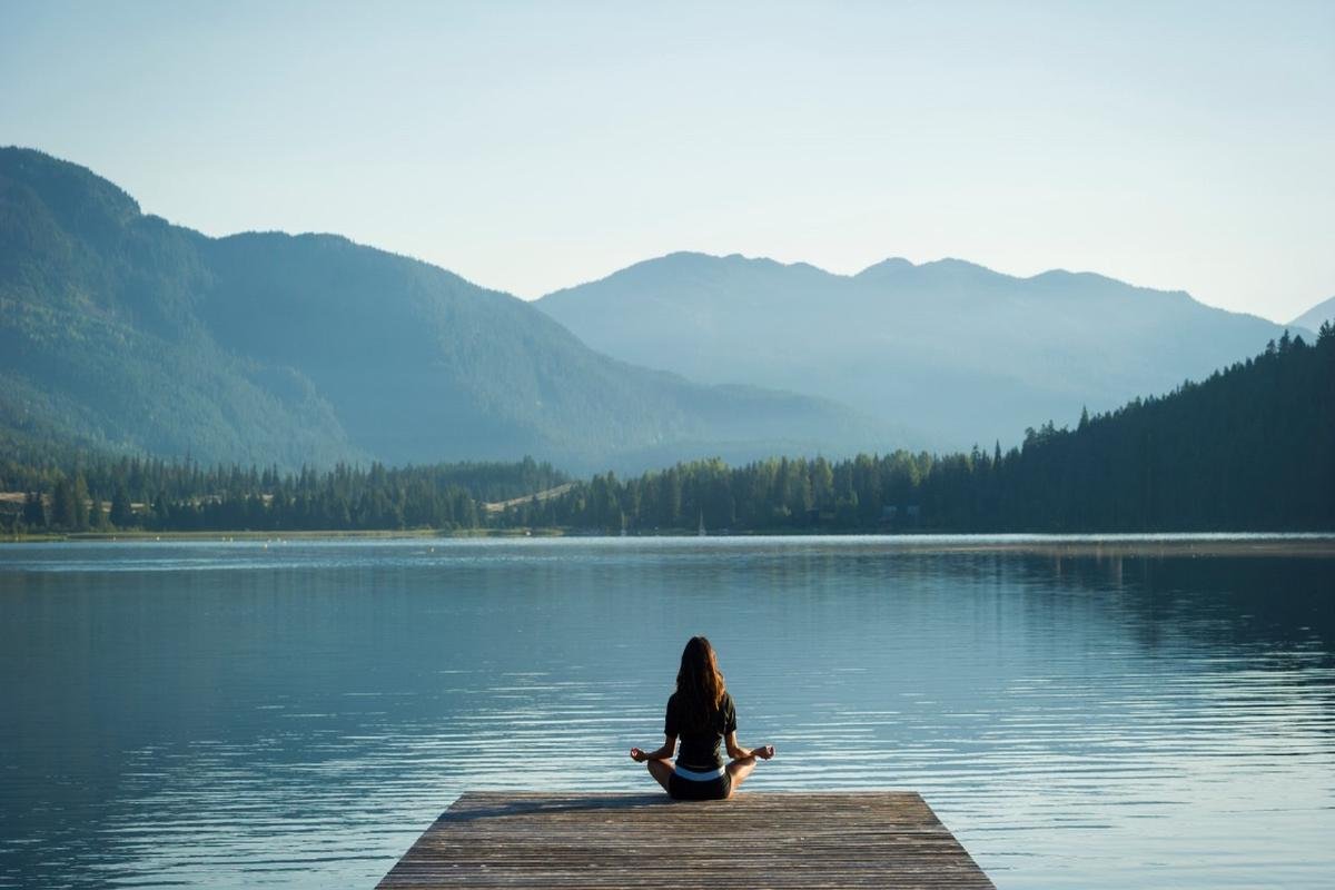Woman meditating by a peaceful lake with mountains in the background – self-help tools for mental wellness and stress relief