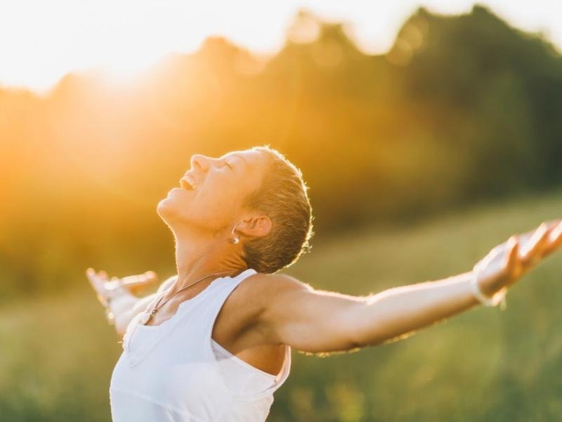 Happy woman enjoying sunlight with open arms, symbolizing freedom, confidence, and positive affirmations for mental well-being.
