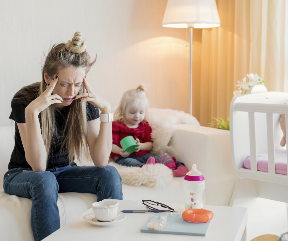 Emotionally exhausted mother sitting on the couch with her child in the background, symbolizing the mental toll of parenting stress and burnout.