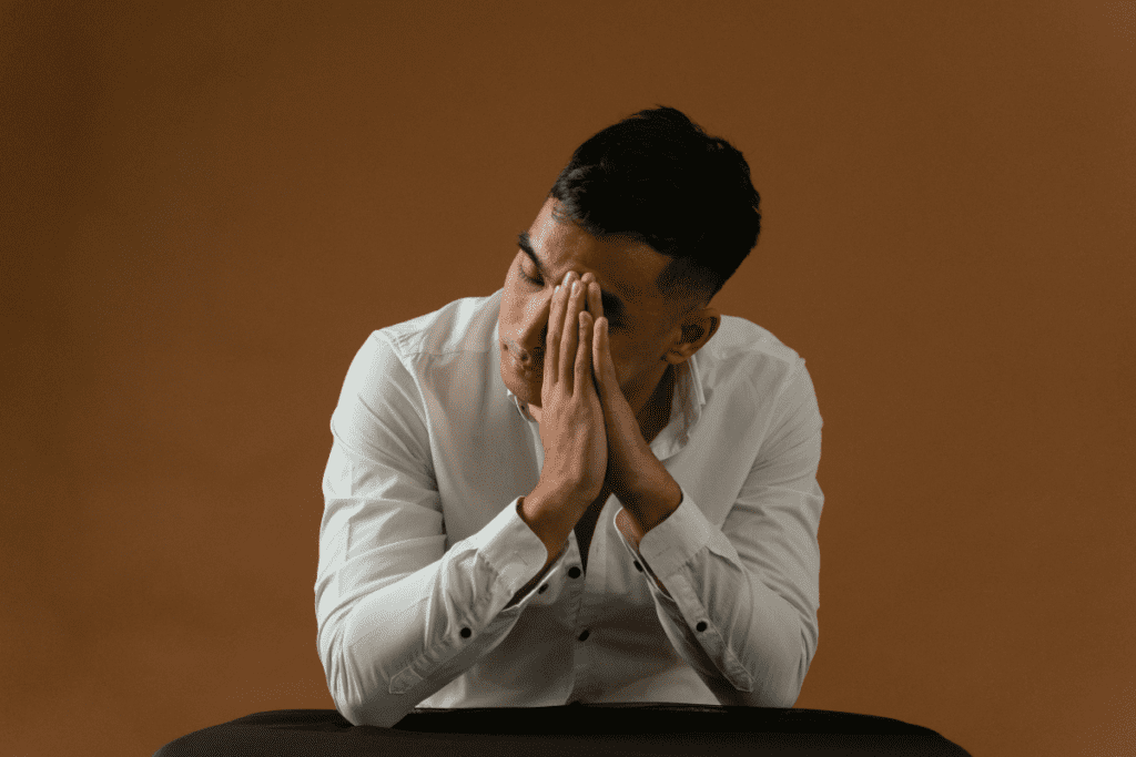 A distressed man sitting with his hands pressed against his face, symbolizing emotional numbness or deep mental exhaustion.
