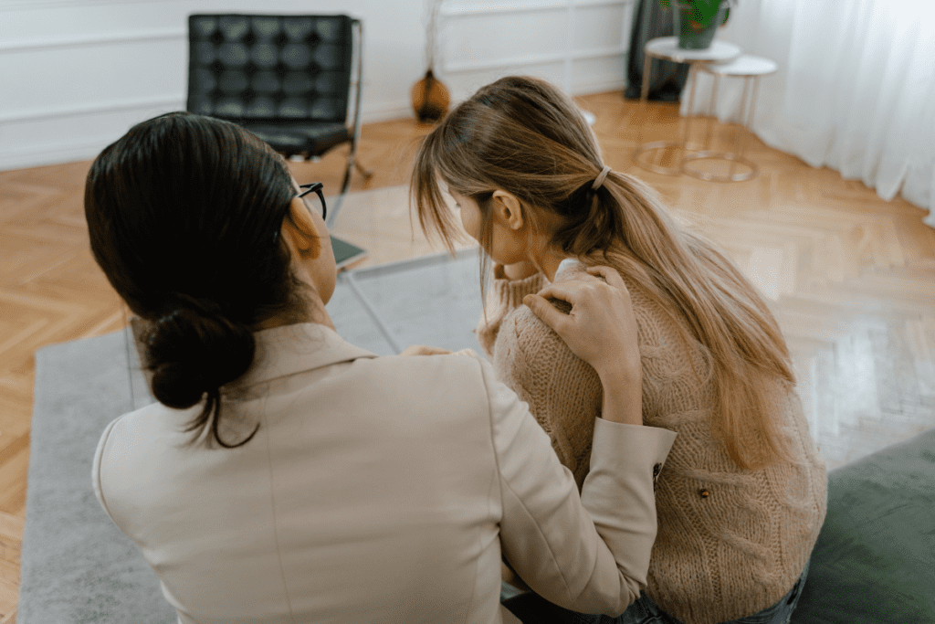 A comforting moment between two women, with one offering emotional support by gently placing her hand on the other’s shoulder.