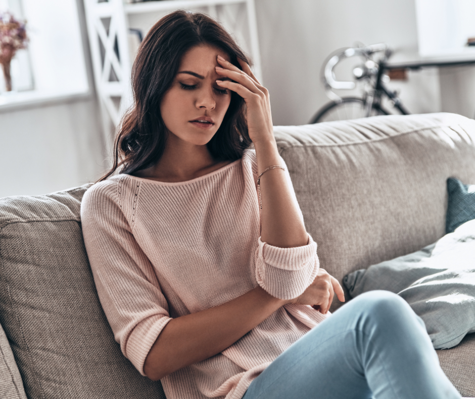 A woman sitting on a couch looking emotionally exhausted and mentally overwhelmed, representing signs of emotional burnout.