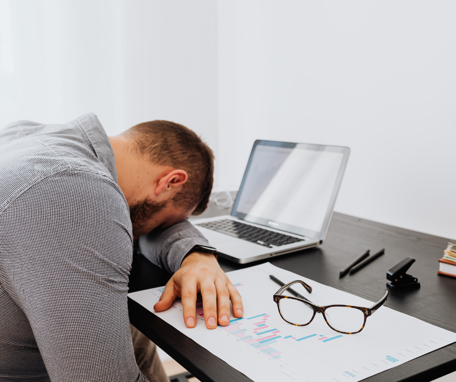 A stressed man resting his head on a desk, overwhelmed with work and mental fatigue, symbolizing emotional exhaustion.
