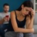 A couple sitting apart on a bed, showing emotional tension and resentment in their relationship.Let Go of Resentment in Relationships