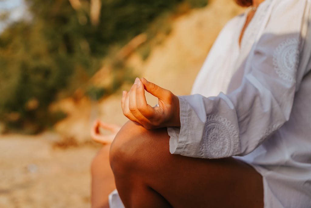 Close-up of a person's hands in a meditative position, practicing mindfulness outdoors at the beach during golden hour.