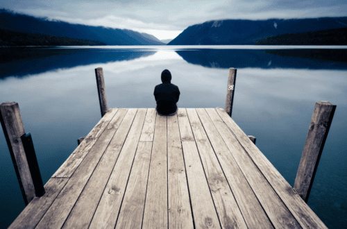 A person sitting alone on a wooden pier, reflecting in silence by a calm lake—capturing the essence of solitude and creativity in nature.