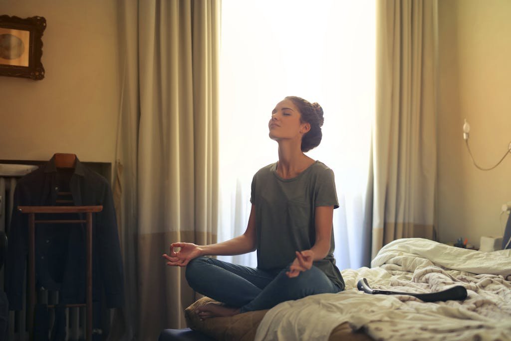 Adult woman practicing meditation on her bed surrounded by a calm bedroom atmosphere as a Self-care for mental wellness