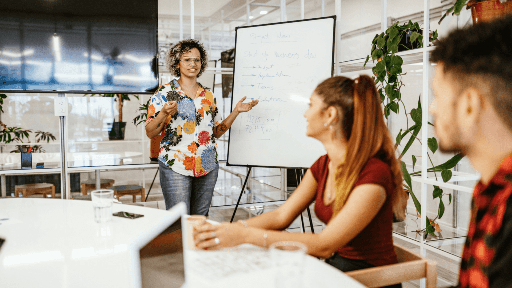 Confident woman giving a presentation to colleagues, showing how to develop charisma through body language and communication skills in a modern office setting.