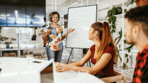 Confident woman giving a presentation to colleagues, showing how to develop charisma through body language and communication skills in a modern office setting.