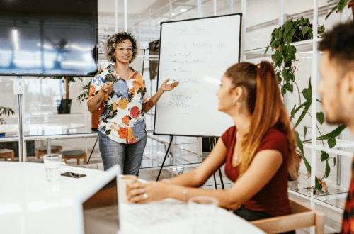 Confident woman giving a presentation to colleagues, showing how to develop charisma through body language and communication skills in a modern office setting.
